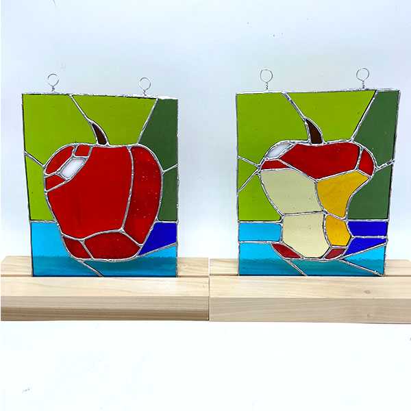 Two stained glass rectangles. One depicts a red apple, the other an apple core.